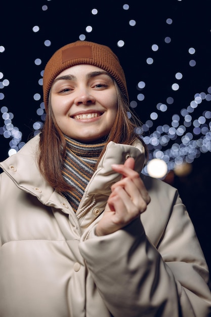 Portrait of happy woman in warm outerwear showing love sign or heart gesture with fingers in winter 