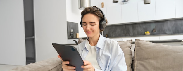 Portrait of happy woman watching video on tablet in headphones working from home using her digital