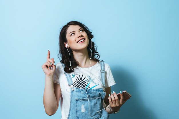 Portrait of happy woman wearing earphones singing isolated over blue wall