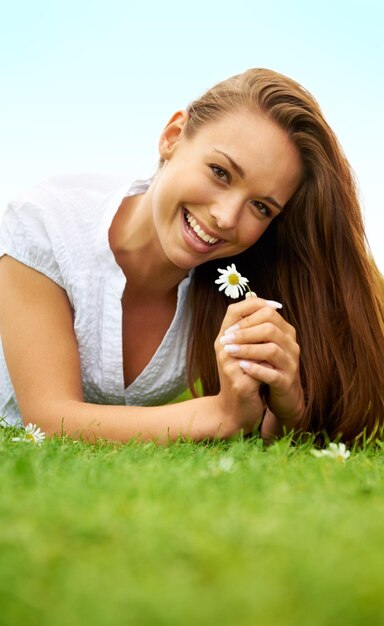 Portrait happy and woman with daisy on grass lying down on field and enjoying spring on vacation outdoor Smile flower plant and beauty of female person relaxing mockup and having fun in nature