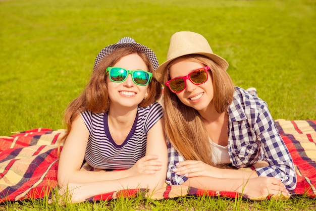 Портрет счастливых женщин в летних шляпах и очках, лежащих на пледе в парке