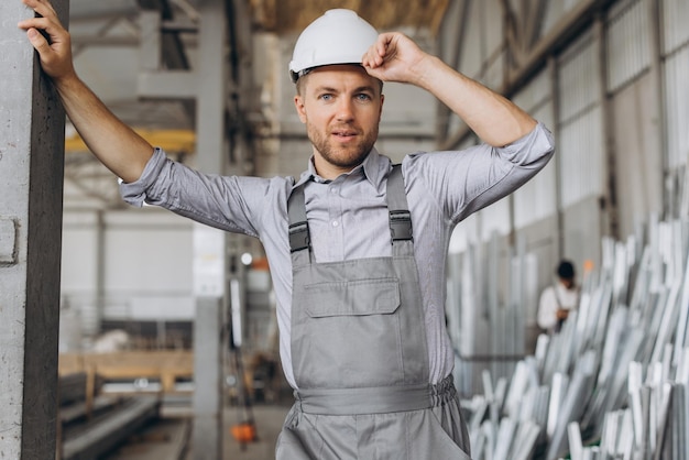 Portrait of a happy worker in a gray uniform and a white hard hat posing on the background of factory production