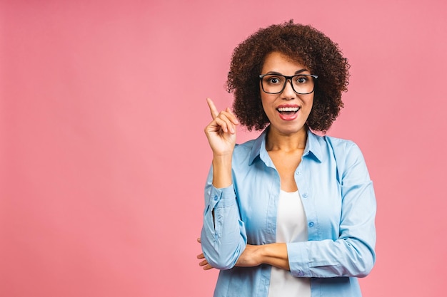 Portrait of a happy young african american black business woman pointing fingers up at copy space isolated over pink background