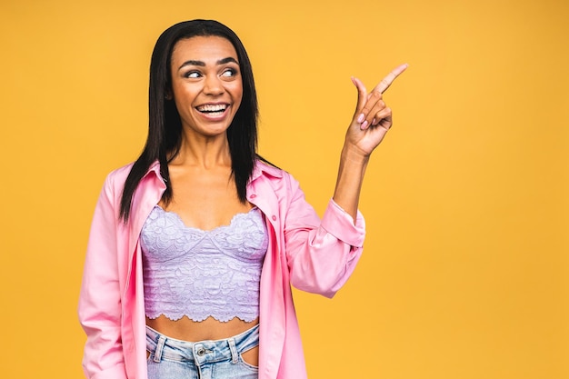 Portrait of a happy young african american woman pointing fingers away at copy space isolated over yellow background