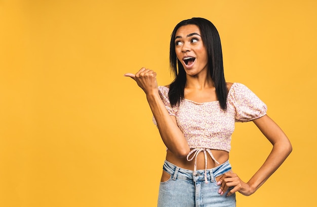 Portrait of a happy young african american woman pointing fingers away at copy space isolated over yellow background