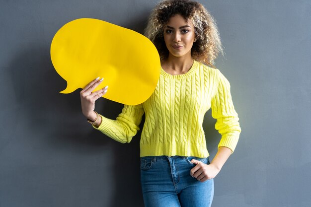 Photo portrait of a happy young african woman holding empty speech bubble isolated over gray background.