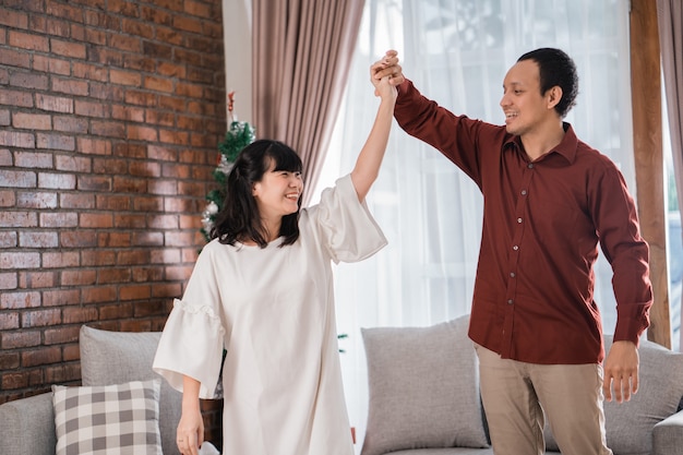 Portrait of happy young asian couple enjoy their time together by dancing in christmas day at home