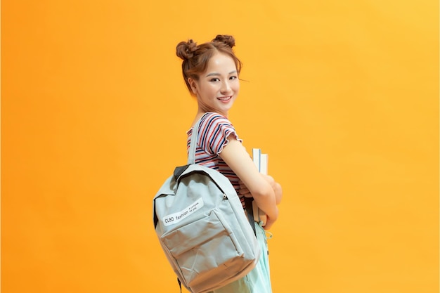 Portrait of a happy young asian female student on yellow background