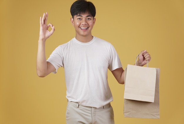 Portrait of happy young asian man dressed casually holding shopping bags isolated