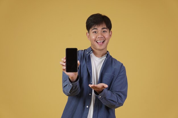 Portrait of happy young asian man dressed casually smiling showing smartphone blank white screen isolated