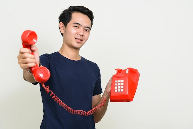 Portrait of happy young Asian man giving old telephone