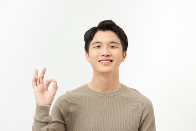 Portrait of happy young asian man smiling and posing with cheerful and okey hand sign