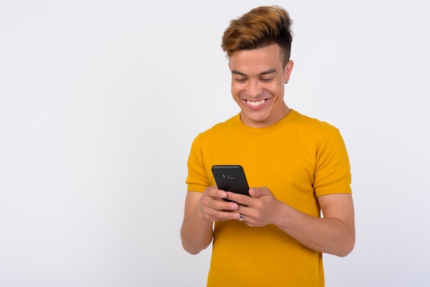 Portrait of happy young Asian man using phone against white wall