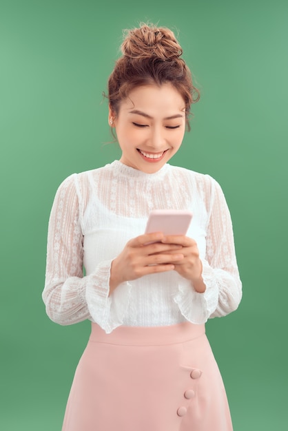 Portrait of happy young Asian woman holding smartphone over green background.