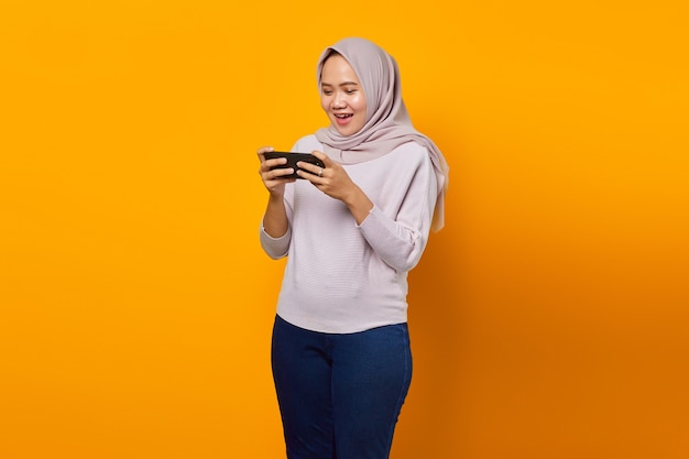 Portrait of happy young asian woman playing video game on mobile phone