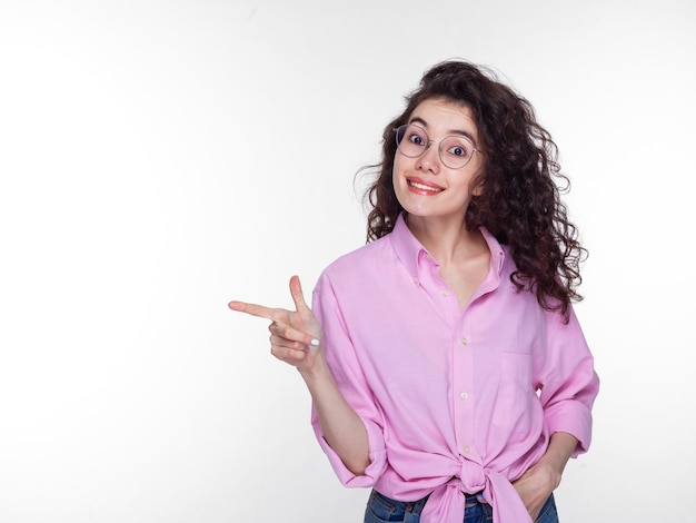 Portrait of a happy young Asian woman standing isolated against a white wall in the studio. The looking camera shows how the copy space points.