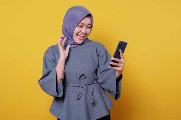 Portrait of a happy young asian woman talking with mobile phone isolated over yellow background