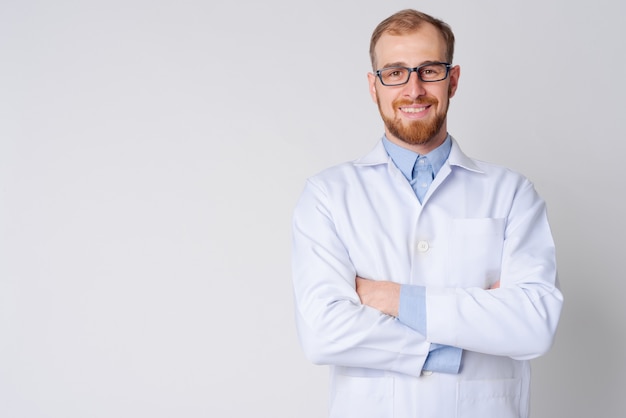 Portrait of happy young bearded man doctor wearing eyeglasses with arms crossed