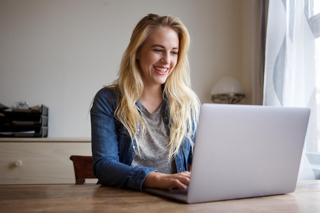 Portrait of happy young blond woman using laptop at home