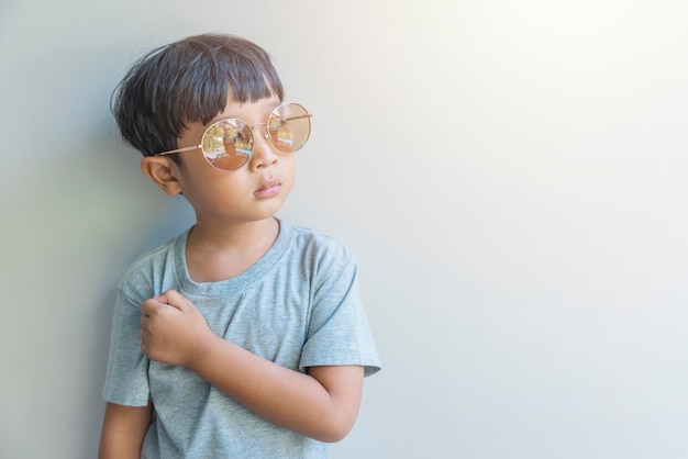 Portrait of a happy young boy of Asia origin in a gray shirt and sunglasses look at the camera