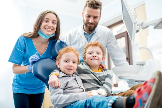 Portrait of happy young boys sitting on the chair with dentist and woman assistant at the dental office