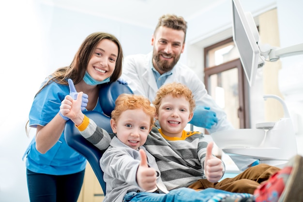 Photo portrait of happy young boys sitting on the chair with dentist and woman assistant at the dental office