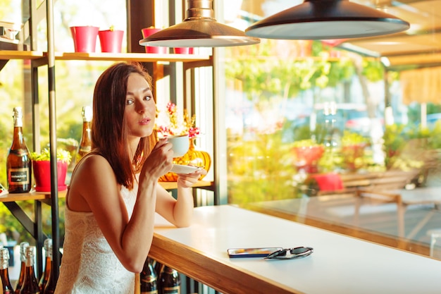 Portrait of happy young business woman with mug in hands drinking coffee at restaurant