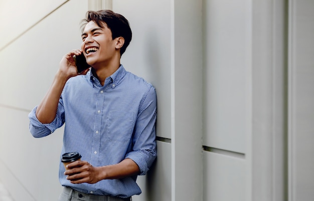 Portrait of a Happy Young Businessman Using Mobile Phone. Lifestyle of Modern People. Standing by the Wall with Coffee Cup