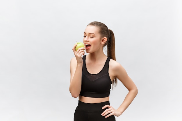 Portrait of a happy young caucasian woman holding and eating green apple  