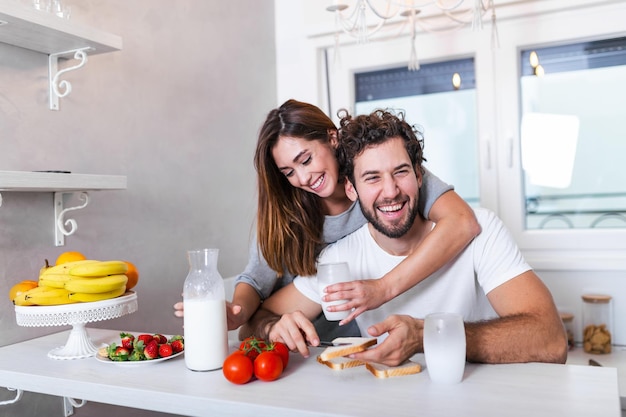 Portrait of happy young couple cooking together in the kitchen at home. Cute young couple enjoying their breakfast together she is pouring him milk wile