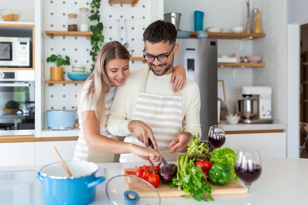집에서 부엌에서 함께 요리하는 행복한 젊은 커플의 초상화 낭만적인 매력적인 젊은 여성과 잘생긴 남자가 밝은 현대식 주방에 서서 함께 시간을 보내고 있다