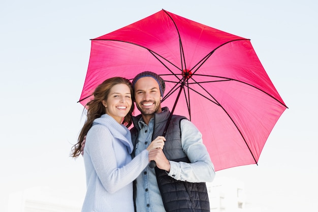 Portrait of happy young couple holding pink umbrella together outdoors