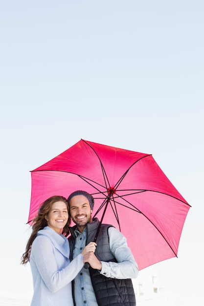 Portrait of happy young couple holding pink umbrella together