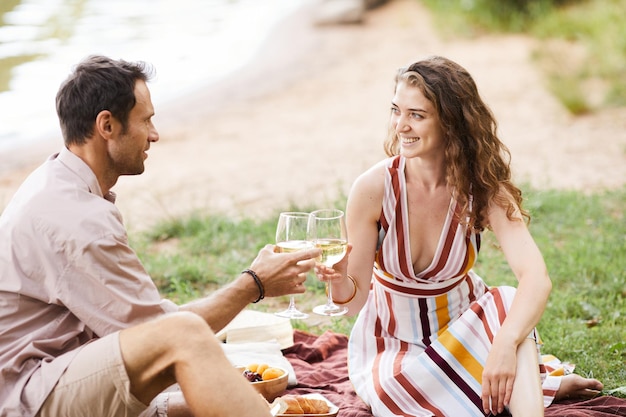 Portrait of happy young couple holding wine glasses while enjoying romantic picnic outdoors copy space