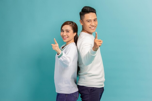 Portrait of happy young couple man and woman smiling and pointing fingers at camera isolated over blue background