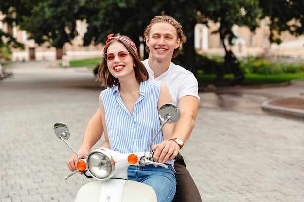 街の通りで一緒にバイクに乗って幸せな若いカップルの肖像画