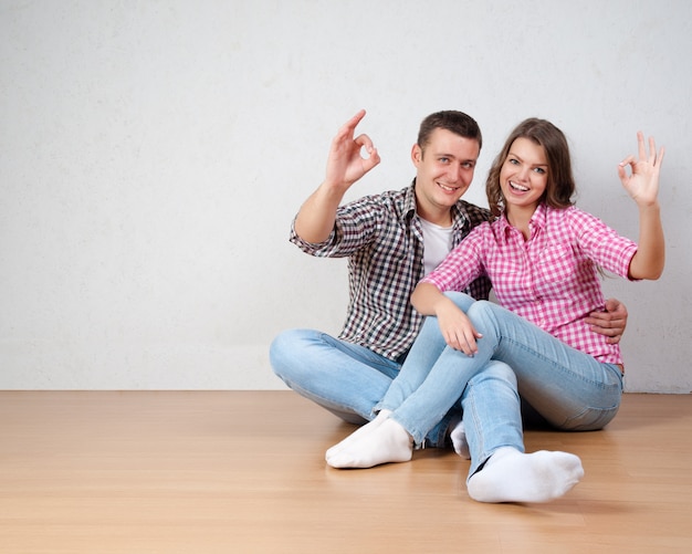 Portrait Of Happy Young Couple Sitting On Floor Looking Up Ready for your text or product