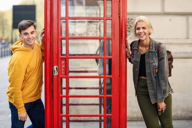 Portrait of happy young couple standing by telephone booth in city