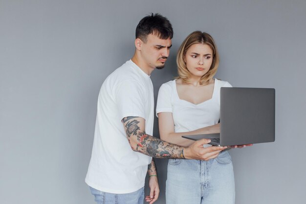 Портрет счастливой молодой пары с ноутбуком на сером фоне