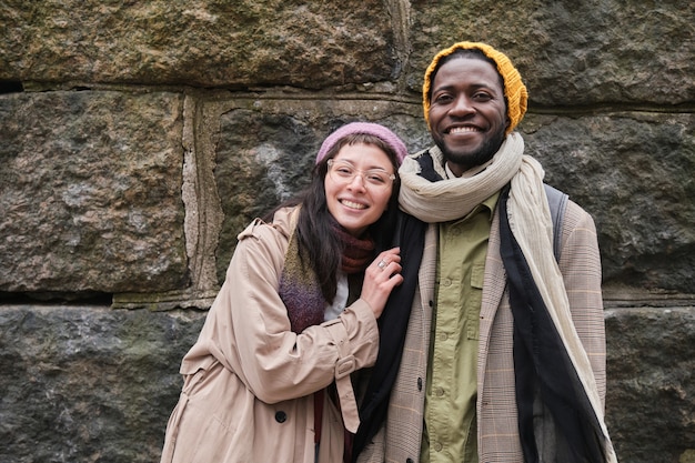 Portrait of happy young couple in warm clothing smiling at camera standing in the city