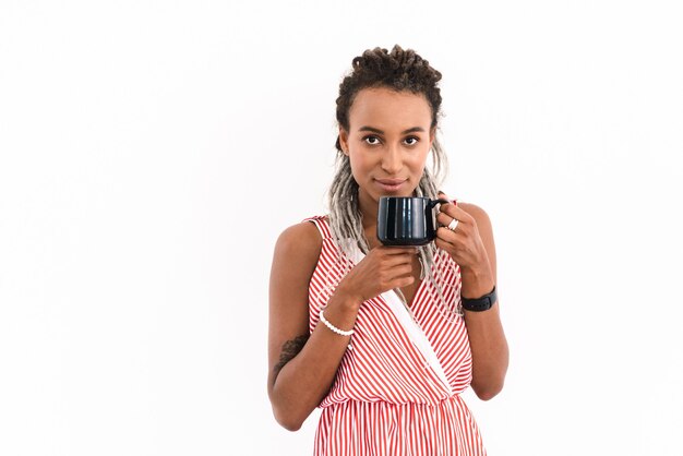 Portrait of a happy young cute cheery woman with dreads posing isolated on white drinking coffee or tea.