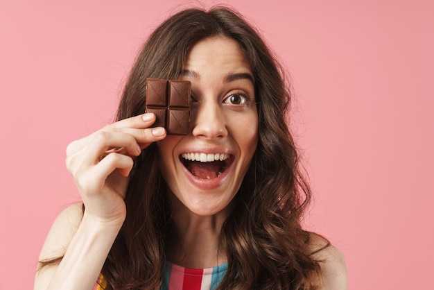 Portrait of a happy young cute woman posing isolated over pink wall holding chocolate sweeties