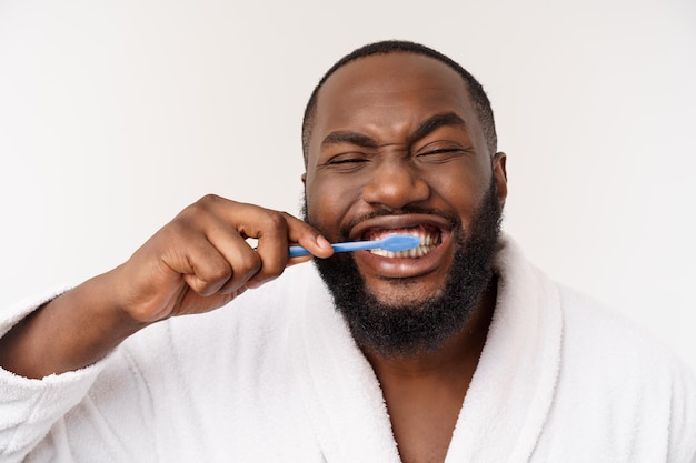 Portrait of a happy young darkanm brushing his teeth with black toothpaste on a white background