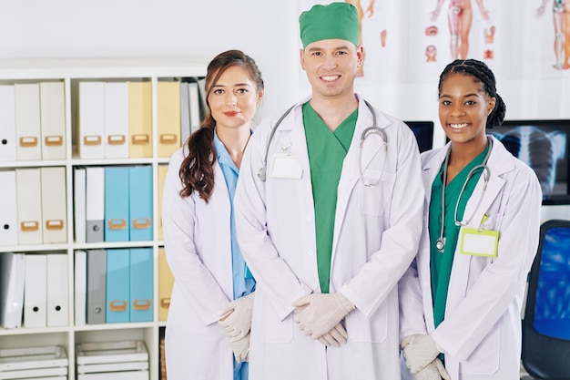 Портрет счастливых молодых врачей, стоящих в медицинском кабинете и улыбающихся спереди