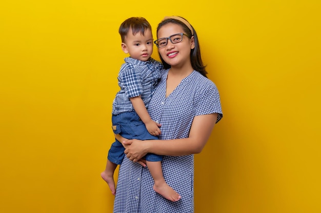 Portrait of happy young family mother keeps in arms tender embracing gently hugging child kid son boy on yellow background Mother's Day parenthood childhood concept