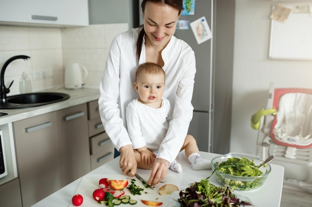 Portrait of happy young family of mother and newborn child spending time together in weekend morning cooking lunch for father