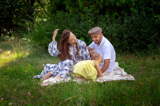 Portrait of happy young family plays with their liitle baby daughter at the green meadow