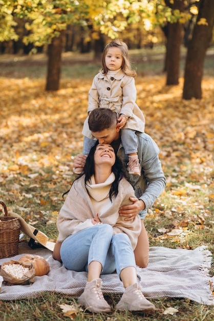 Portrait of happy young family sitting on plaid together in autumn park