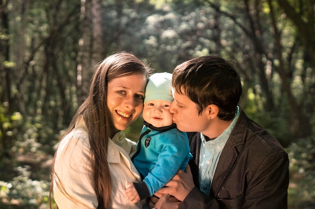 Portrait of a happy young family spending time together in summer nature on vacation in nature Mom and dad hold baby son in their arms and kiss