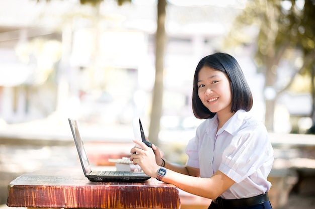 Portrait of a happy young female  student relaxing outdoor with music and laptop